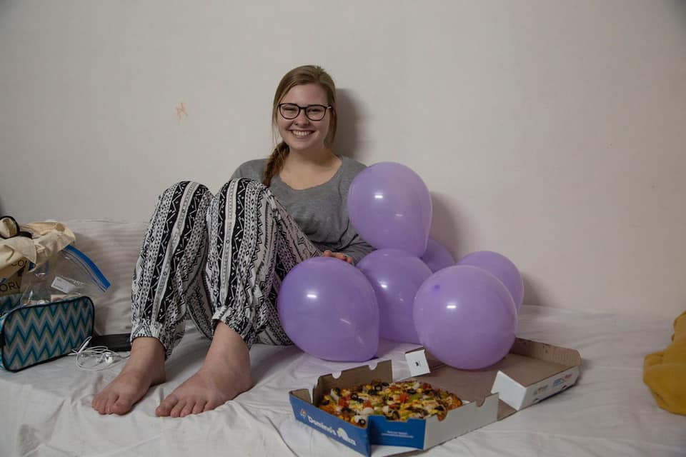 Michelle sitting on a bed with balloons and a pizza